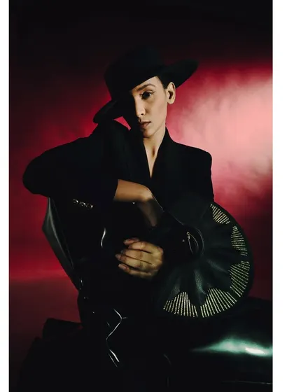 A portrait from the 'Levels of Power' series, where the model is seated against a red backdrop. The lighting is focused and dramatic, highlighting the sharp lines of the blazer and the subject's confident pose.