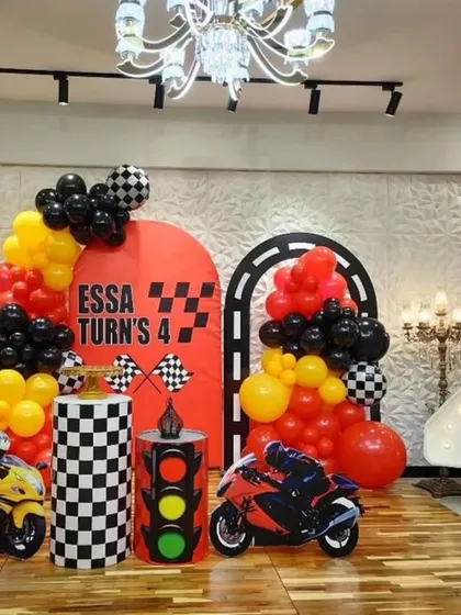 A race car and motorcycle themed party for a 4th birthday. We used red, yellow, and black balloons, checkered flag details, and a large light-up marquee number '4' to create a thrilling atmosphere.