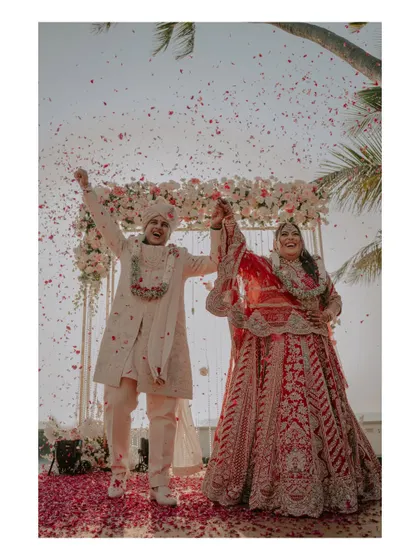 The couple celebrates with hands raised high after their Varmala, showered in petals by their guests.