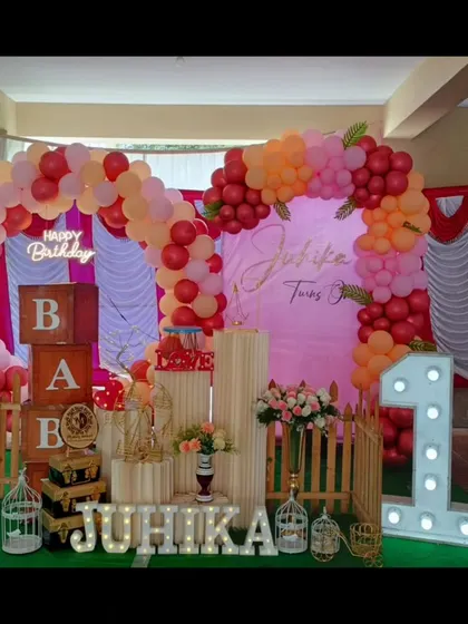 A warm and inviting first birthday setup for Juhika. The red, pink, and orange balloon arch creates a cheerful and bright backdrop.