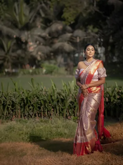 A full-length portrait of the bride in a stunning Kanchipuram saree, set against a lush green backdrop. The golden hour light makes her and the saree glow.