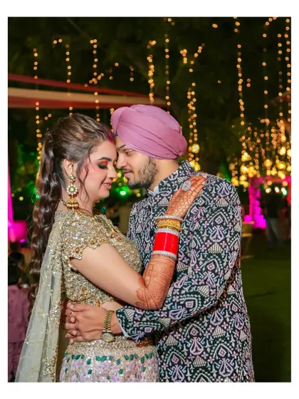An intimate couple portrait against a backdrop of golden fairy lights. The groom's embrace and the bride's happy expression capture a perfect moment of love and celebration.