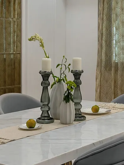 The art of the tablescape. Here, smoked glass candle holders and simple greenery on a white marble table create a look of understated elegance, perfect for any dining occasion.
