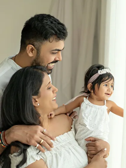 A candid family portrait by the window. The natural light illuminates their happy faces as they share a moment of togetherness.