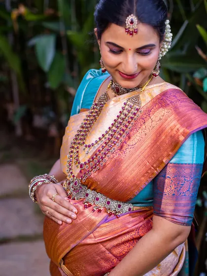 A beautiful close-up portrait of the mother-to-be. Her gentle smile and the way she cradles her bump convey a deep sense of love and connection. The rich colors of her saree pop against the soft, natural background.