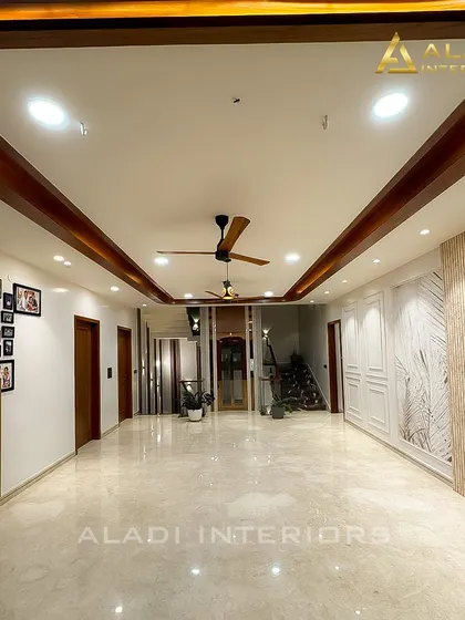 An expansive hallway with marble flooring and a wooden false ceiling. The walls feature a gallery of family photos and elegant paneling, telling the story of the home's residents.