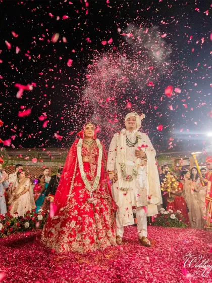 A shower of red rose petals rains down on the couple as they stand hand-in-hand after their wedding ceremony.