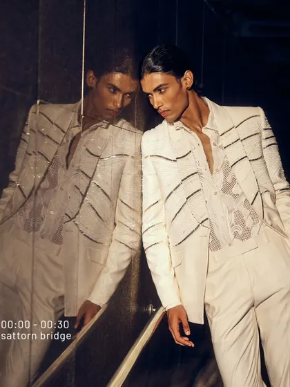 The night begins with a reflection. This white-on-white ensemble features linear beading on the jacket, creating a look that is both textured and clean. It’s a statement of midnight luxury, designed to be unforgettable.