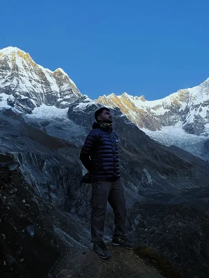 A trekker stands in awe before the glacial moraine and towering peaks of the Annapurna Sanctuary, a landscape that feels otherworldly.