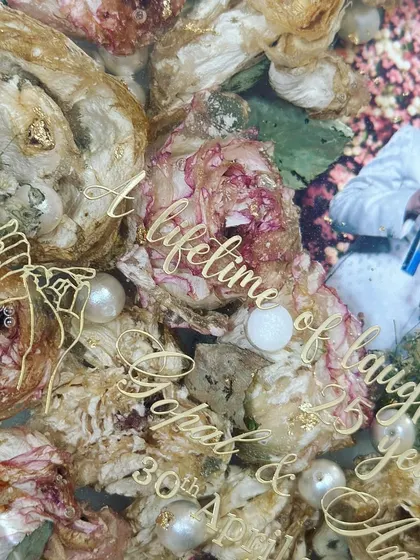 A detailed shot showing the intricate layering of flowers and the custom gold lettering. Every element is carefully placed to create a balanced and beautiful composition.