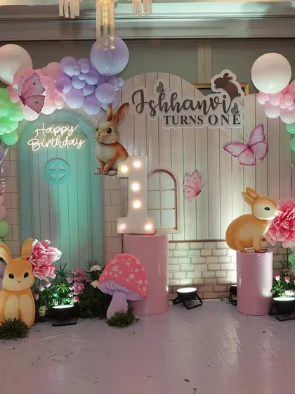 A whimsical bunny-themed backdrop for Ishhanvi's first birthday, featuring pastel balloons, cute bunny figures, and magical mushrooms.