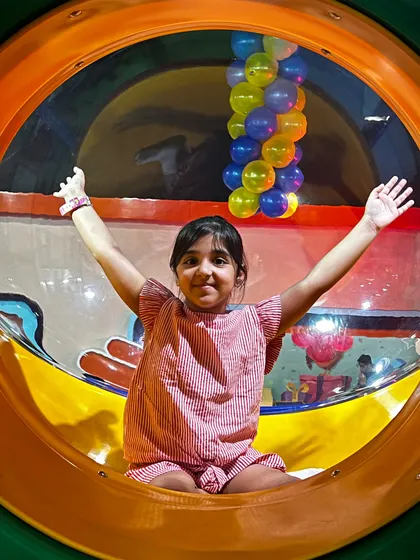 A happy girl peeks out from a transparent tube slide, one of the many exciting ways to travel through our play maze.