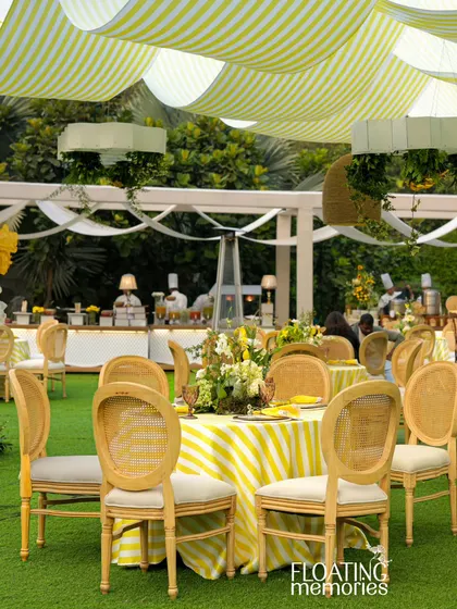 The elegant guest seating arrangement, with striped tablecloths and natural wood caned chairs, perfectly complements the sunny, garden-party vibe of this luxury baby shower.
