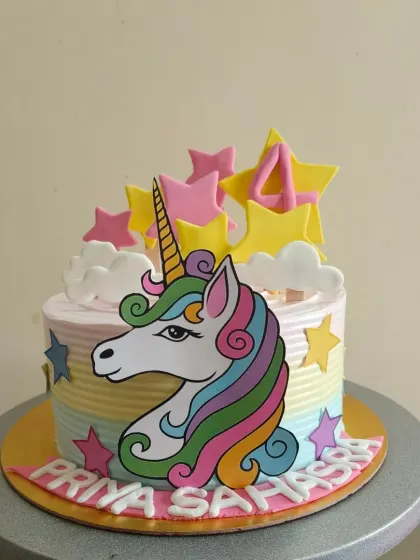 A vibrant unicorn cake with a rainbow striped side and star decorations.