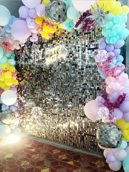 A shimmering sequin wall framed by a colorful pastel balloon arch and disco balls, creating a fun and glamorous photo spot for a sunshine-themed party.