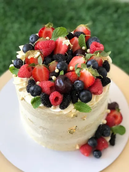 A "naked" cake overflowing with a bounty of fresh mixed berries, including strawberries, blueberries, and raspberries.