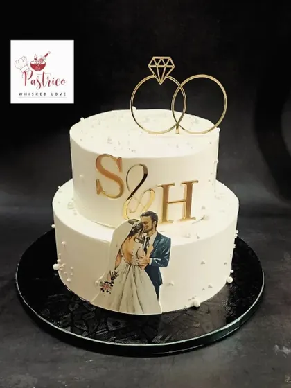 An elegant two-tiered engagement cake with a custom photo, gold monograms, and a beautiful ring topper.