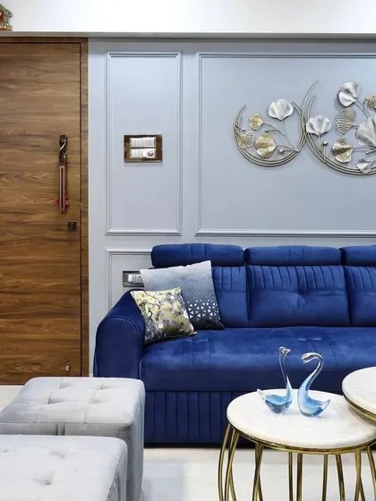 A close-up of a royal blue sectional sofa set against a light grey wall with decorative mouldings. The design is accented with a metallic wall art piece, creating a striking contrast of color and texture.