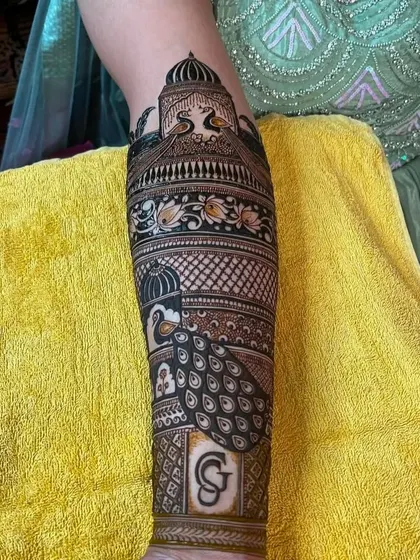 A close-up of a personalized initial 'G' inside a shield on the forearm. This is part of a larger bridal design.