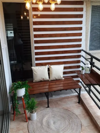 This shot shows the full setup of the classy pinewood balcony, including the bench, wall panelling, and the custom railing table for extra utility. The hanging lamp adds a beautiful finishing touch.