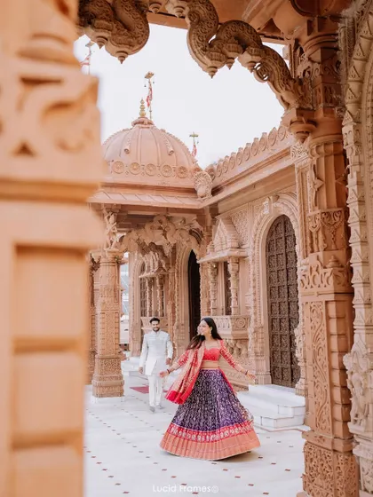 A unique perspective looking through the temple's carved pillars as the bride leads the groom, creating a sense of discovery.