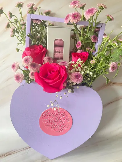 A heart-shaped floral box for Mother's Day. This lovely arrangement includes fresh roses and a box of delicate macarons.