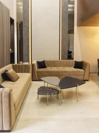 An elegant and subtle living room design with a beige velvet sofa and abstract nested coffee tables. The high ceiling and minimalist decor create a sense of spaciousness and luxury.