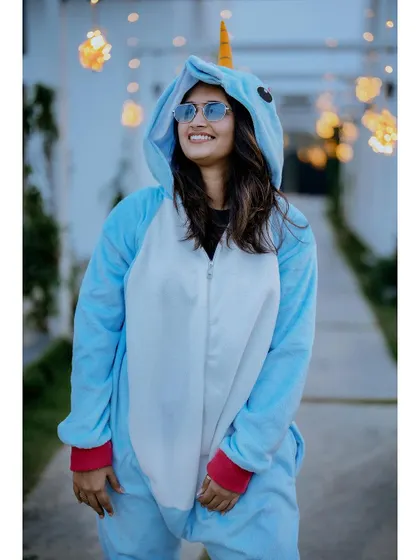 A solo portrait of the bride in her blue unicorn onesie, smiling and looking happy against a backdrop of fairy lights.