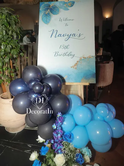The personalized welcome sign for Navya's 15th birthday, decorated with a small balloon cluster in the party's blue and black color scheme.