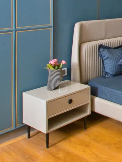 A simple and chic bedside table in a neutral color, paired with a blue upholstered bed and wall panels with gold trim. The design is clean, modern, and elegant.