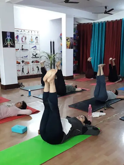 A class practices Urdhva Prasarita Padasana (Upward Extended Feet Pose). This posture is excellent for strengthening the lower abdomen and improving circulation.