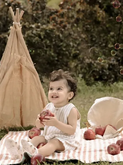 An apple-themed picnic for a first birthday. The birthday boy sits on a blanket with a basket of apples and a cute teepee in the background, creating a charming and natural setting.