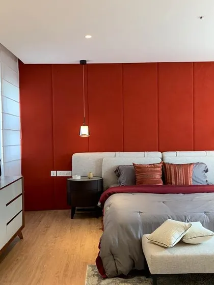 A bold, fabric-paneled wall in deep red acts as a dramatic headboard and feature wall in this bedroom. This use of color and texture adds warmth and a sense of luxury to the space.