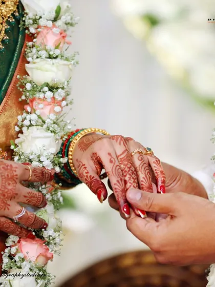 A close-up of the ring ceremony, framed by the couple's beautiful floral garlands. This shot highlights the joining of hands and the start of a new journey.