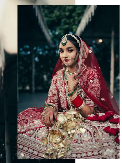 A full-length portrait of the bride seated, showcasing her magnificent lehenga and traditional red bangles. The pose is both regal and serene.