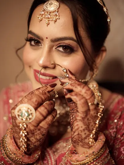 A close-up of the bride playing with her nath. The rose gold makeup looks stunning against her intricate henna.