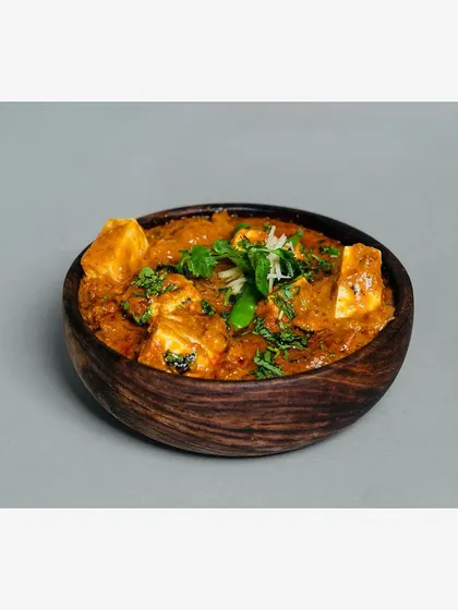 A wooden bowl of paneer butter masala, shot against a clean, neutral grey background. This is a standard product-on-white (POW) style shot, essential for any online menu.