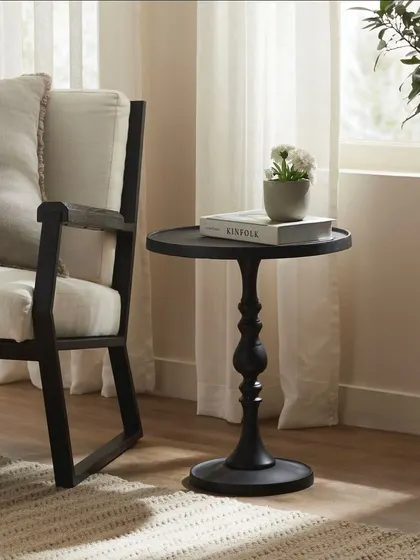 A black pedestal side table from the 'Sotto Bosco' collection, placed next to a modern armchair. This simple, elegant shot highlights the table's sculptural form.