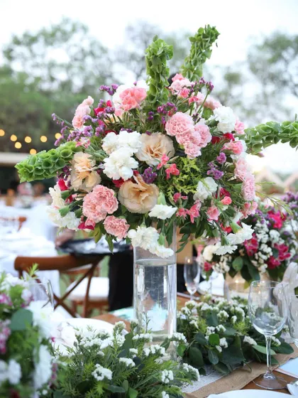 An elegant and lush centerpiece for a dining table. A tall glass vase holds a large bouquet of white and pink carnations with cascading bells of Ireland.