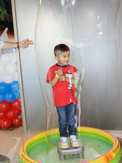 A child stands inside a giant soap bubble, a mesmerizing and unforgettable party activity.