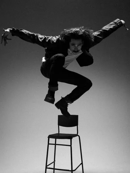 A dynamic shot from the 'Blaze Of Glory' series. The styling is minimalist rock-and-roll with a black jacket and jeans, allowing the focus to be on the model's athletic movement and the dramatic lighting.