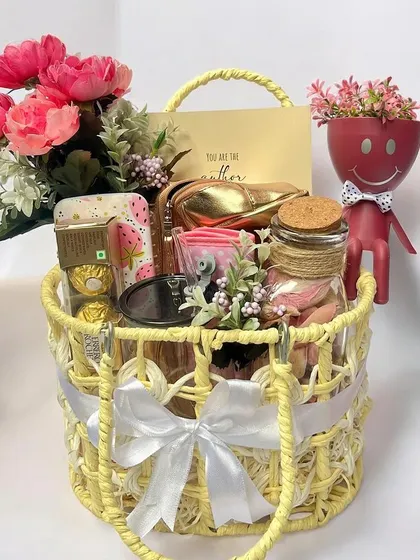 A cheerful yellow-themed gift basket perfect for celebrating a special bond. It's filled with curated items and adorned with pink flowers, a white ribbon, and a cute smiley-faced planter.