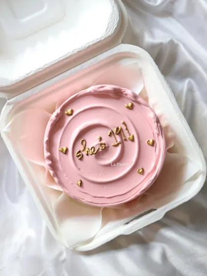 A pretty pink bento cake for a 21st birthday, with 'She's 21!' written in gold and surrounded by tiny gold hearts.