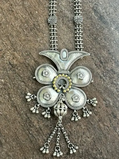 A unique oxidised silver pendant with a touch of gold. This large, floral-inspired piece has beautiful texture and detail, with dangling silver beads that add movement.