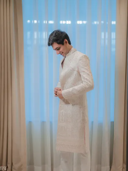 A candid shot of the groom smiling as he adjusts his elegant white sherwani.