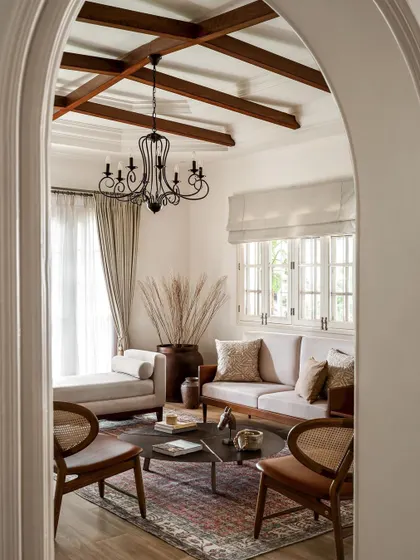 An arched view into the formal living room, where I designed a space with soaring ceilings and classic details. The exposed wooden beams and antique-style chandelier evoke a sense of grandeur, while the comfortable, modern furniture makes it feel livable.