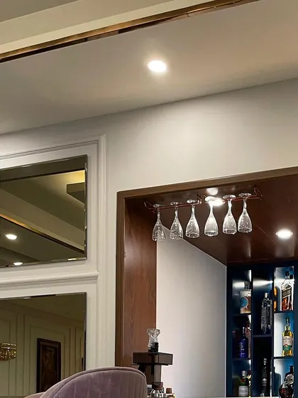 A detail shot of the bar area, showing the overhead glass hangers and the rich wooden finish of the bar niche. The design is integrated seamlessly with the home's overall aesthetic.