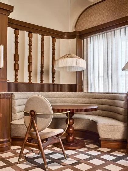 A cozy dining nook at One8 Commune, featuring a curved banquette and a custom chair with a distinctive circular backrest. The design combines rich wood textures with soft upholstery and fringed lighting, crafting an intimate corner within the larger restaurant.