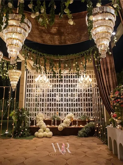 The entrance to the main event area, framed by brown velvet drapes and hanging greenery. The space is filled with chandeliers and features a custom white jaali backdrop.