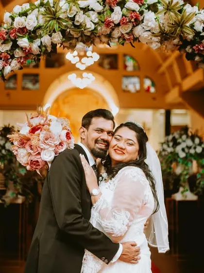 A happy portrait of the newlyweds under a beautiful floral arch at the church entrance.